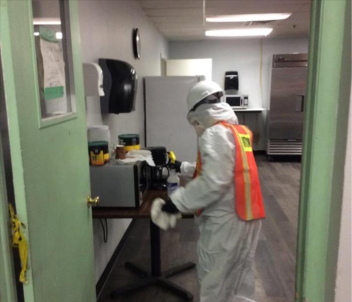 technician wearing white bodysuit, gloves, mask, and hardhat cleaning microwave